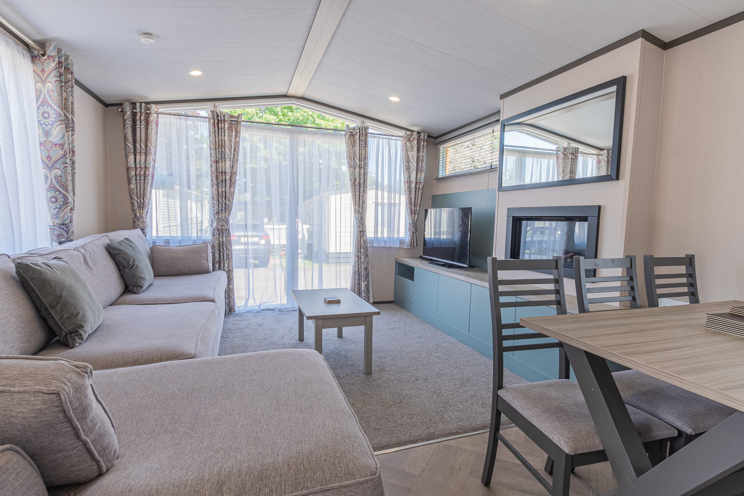 Oakcliff's Lapwing Mini Lodge open-plan living area. Including a large family-style sofa, dining table and built-in fire.