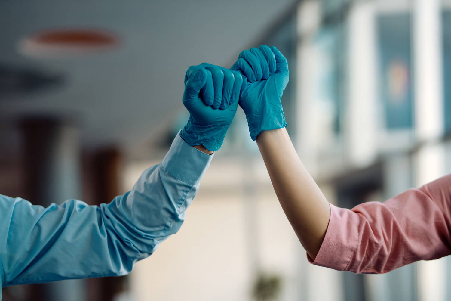 Two people wearing blue gloves, fist-bumping
