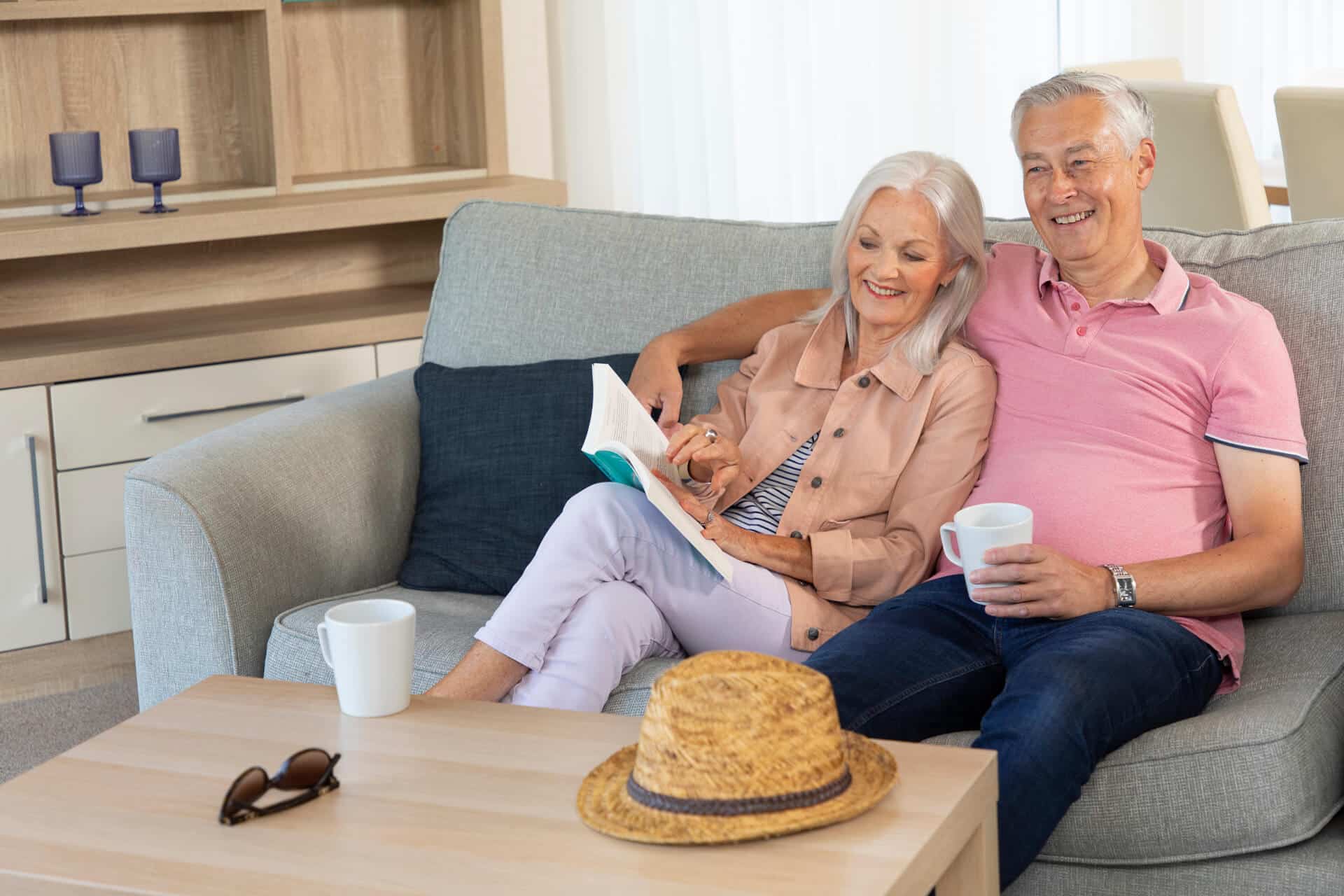 An elderly couple hugging on the sofa. The woman is reading