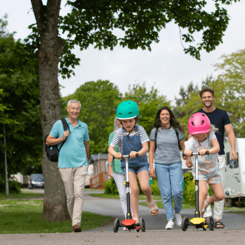 Smiling adults walking behind their children who are on scooters