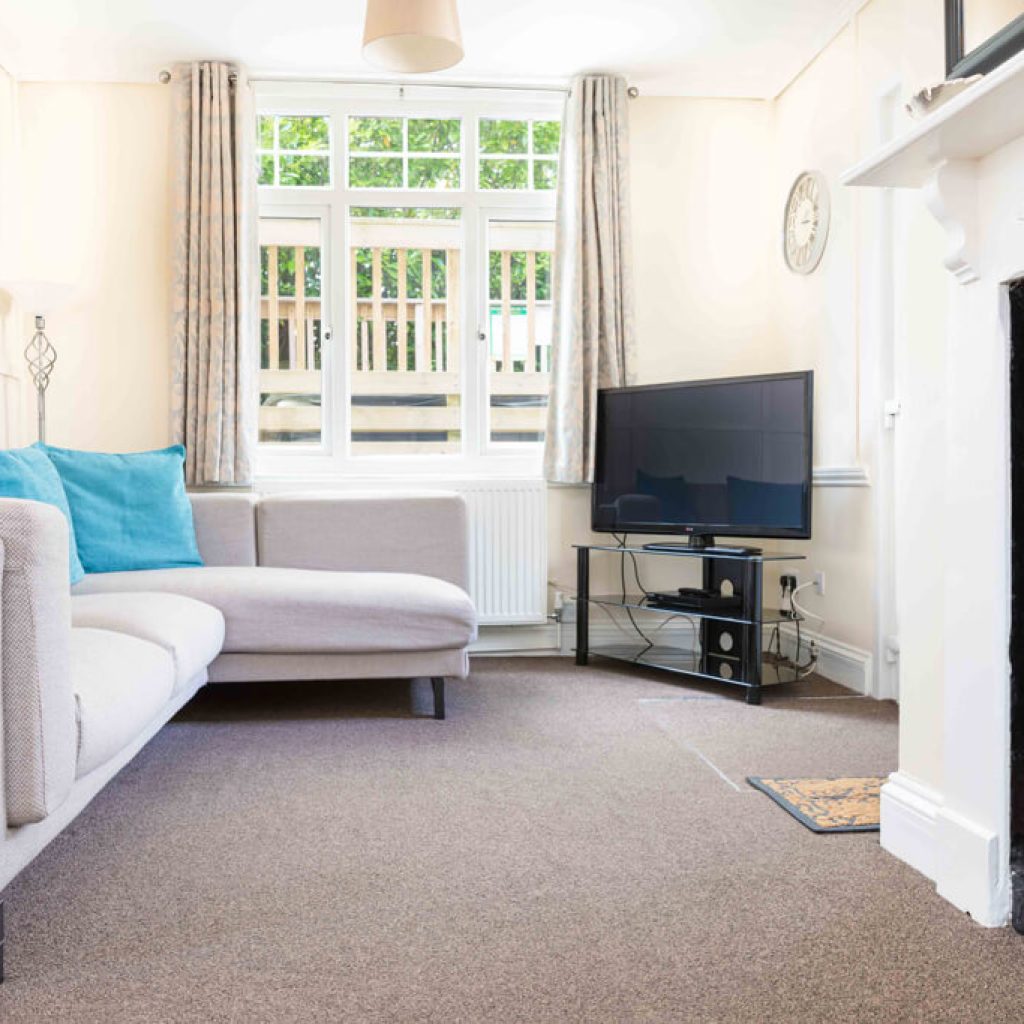 Oakcliff's Oak Cottage living room. With large windows, an L-shape sofa and TV.