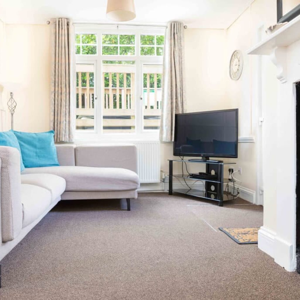 Oakcliff's Oak Cottage living room. With large windows, an L-shape sofa and TV.