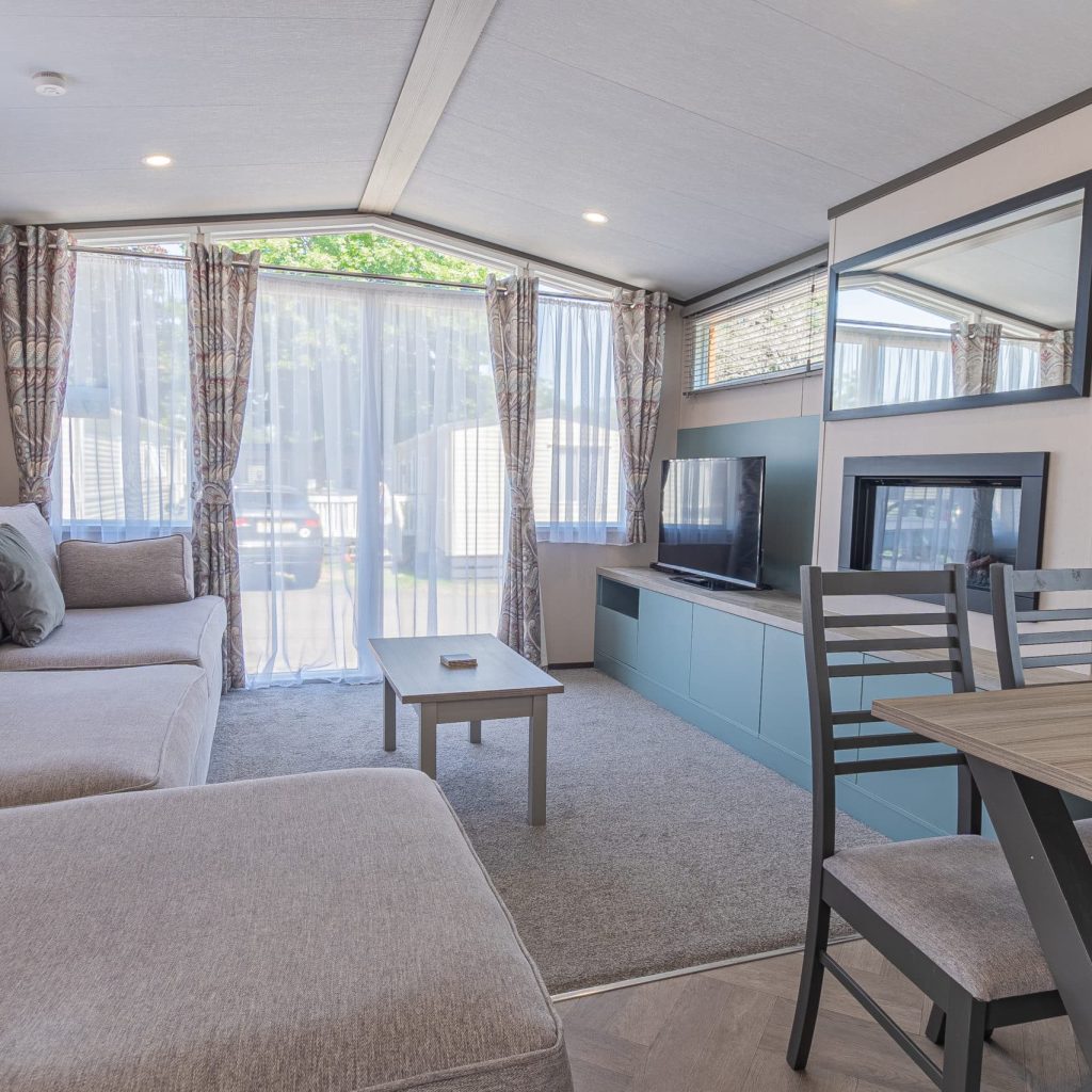 Oakcliff's Lapwing Mini Lodge open-plan living area. Including a large family-style sofa, dining table and built-in fire.