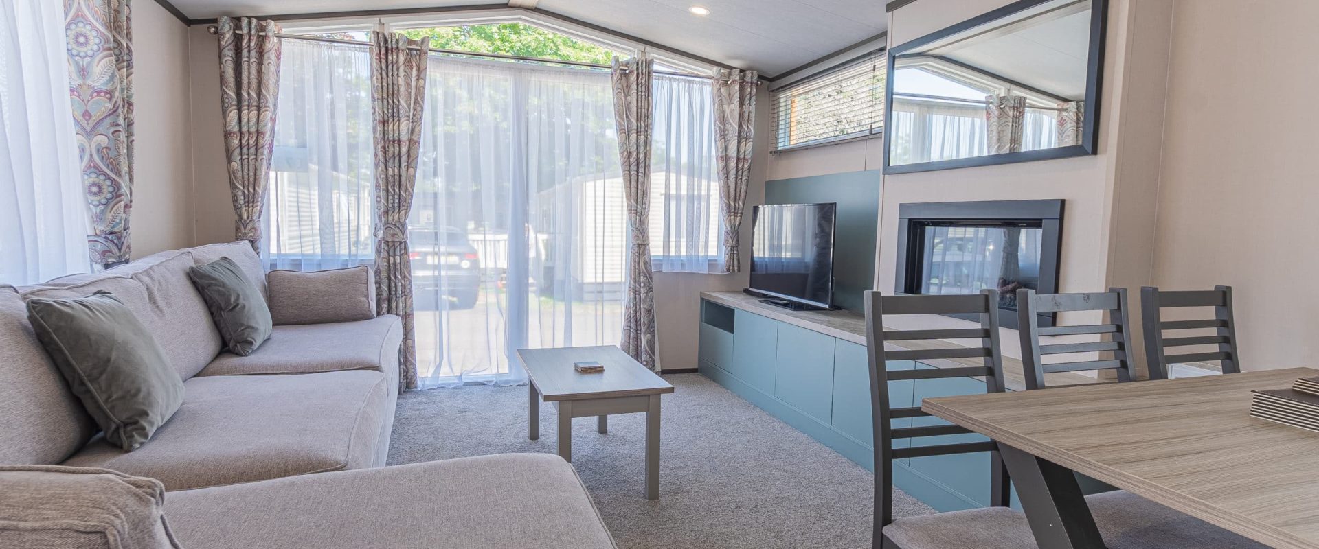 Oakcliff's Lapwing Mini Lodge open-plan living area. Including a large family-style sofa, dining table and built-in fire.