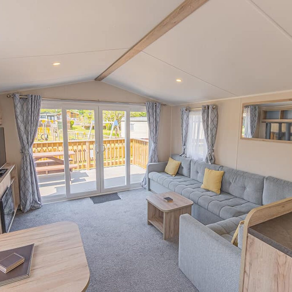Oakcliff's Wren Plus Caravan spacious living room with a large, family-style sofa, glass doors to access the pravte decking and a TV.