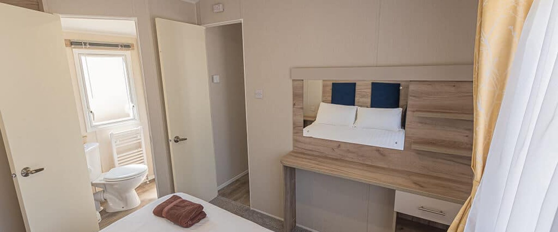 Oakcliff's Wren Plus Caravan double bedroom with a wall-mounted mirror